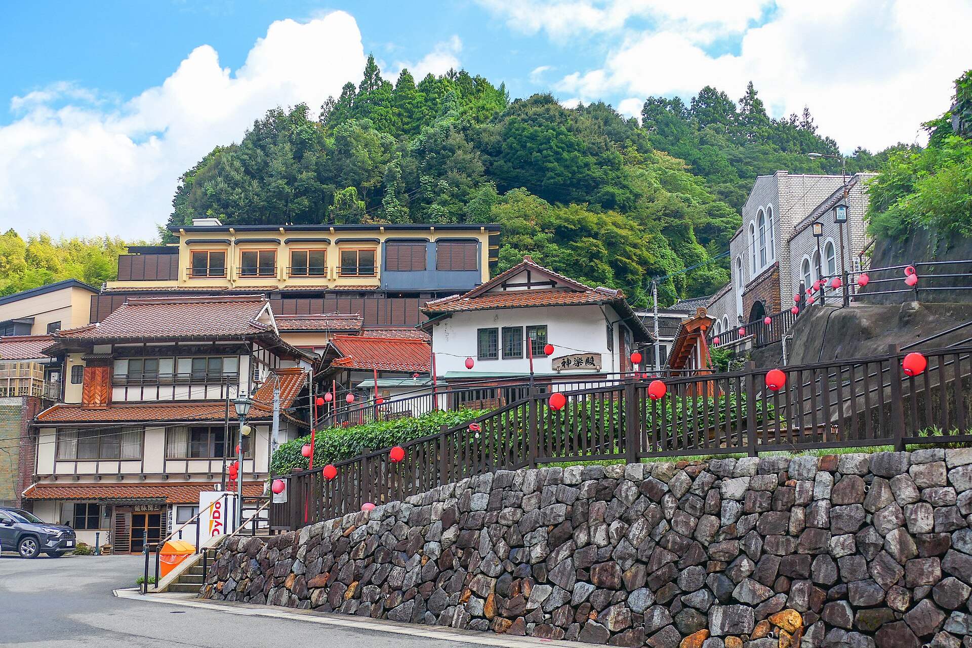 有福温泉の中心部。石垣と赤い提灯の坂道、山あいに建つ旅館と御前湯