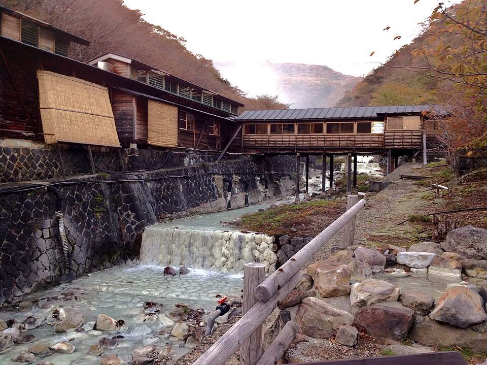 那須温泉の鹿の湯の木造の建物と白濁した湯の流れる湯川