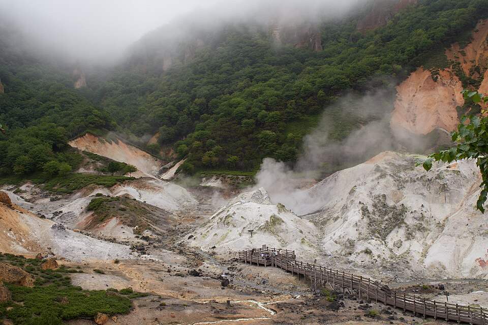 登別温泉の地獄谷。白い噴気地帯から湯けむりが上がり、木道が通る