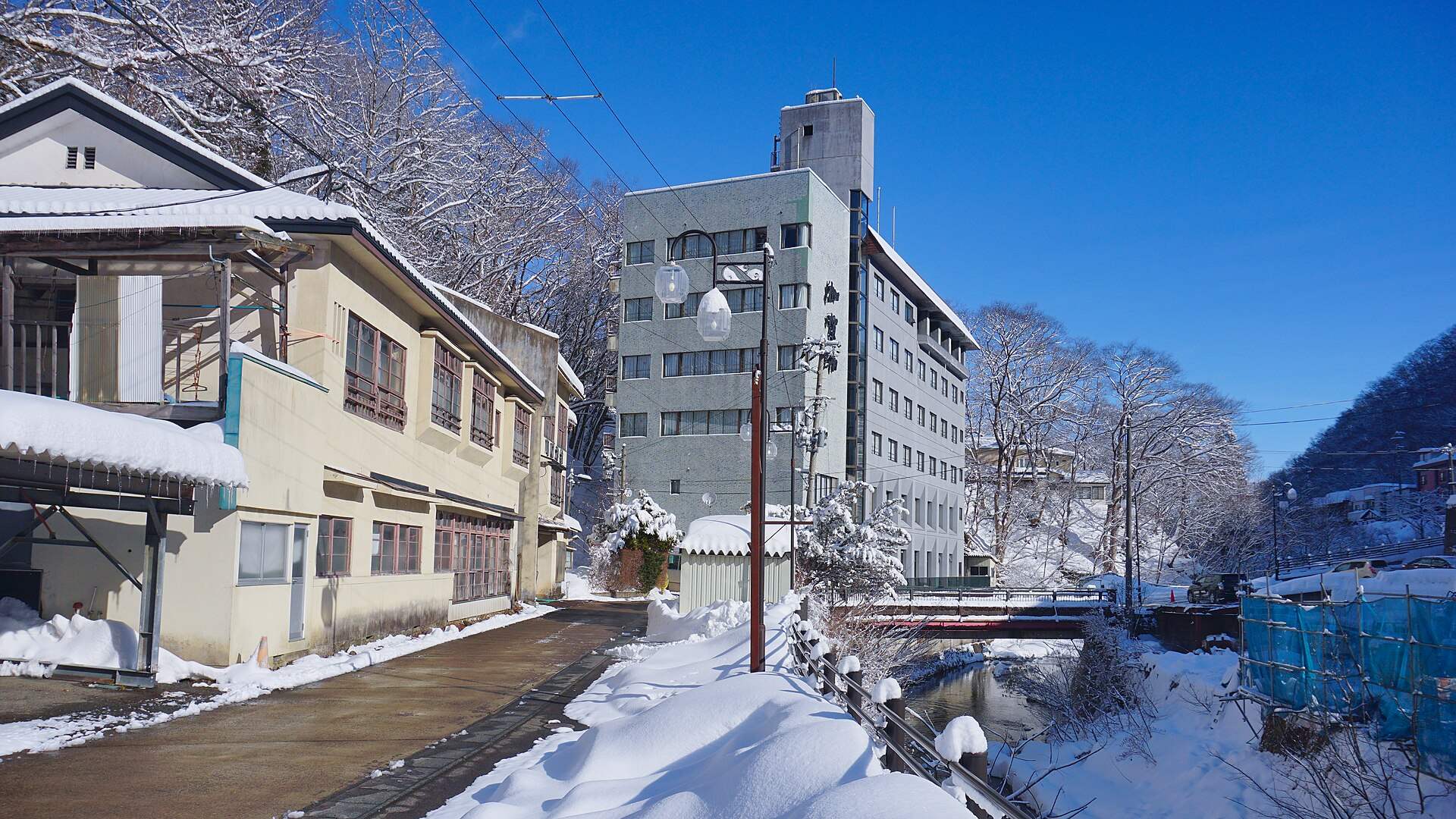 雪の鶯宿温泉。川沿いの道と温泉街の建物