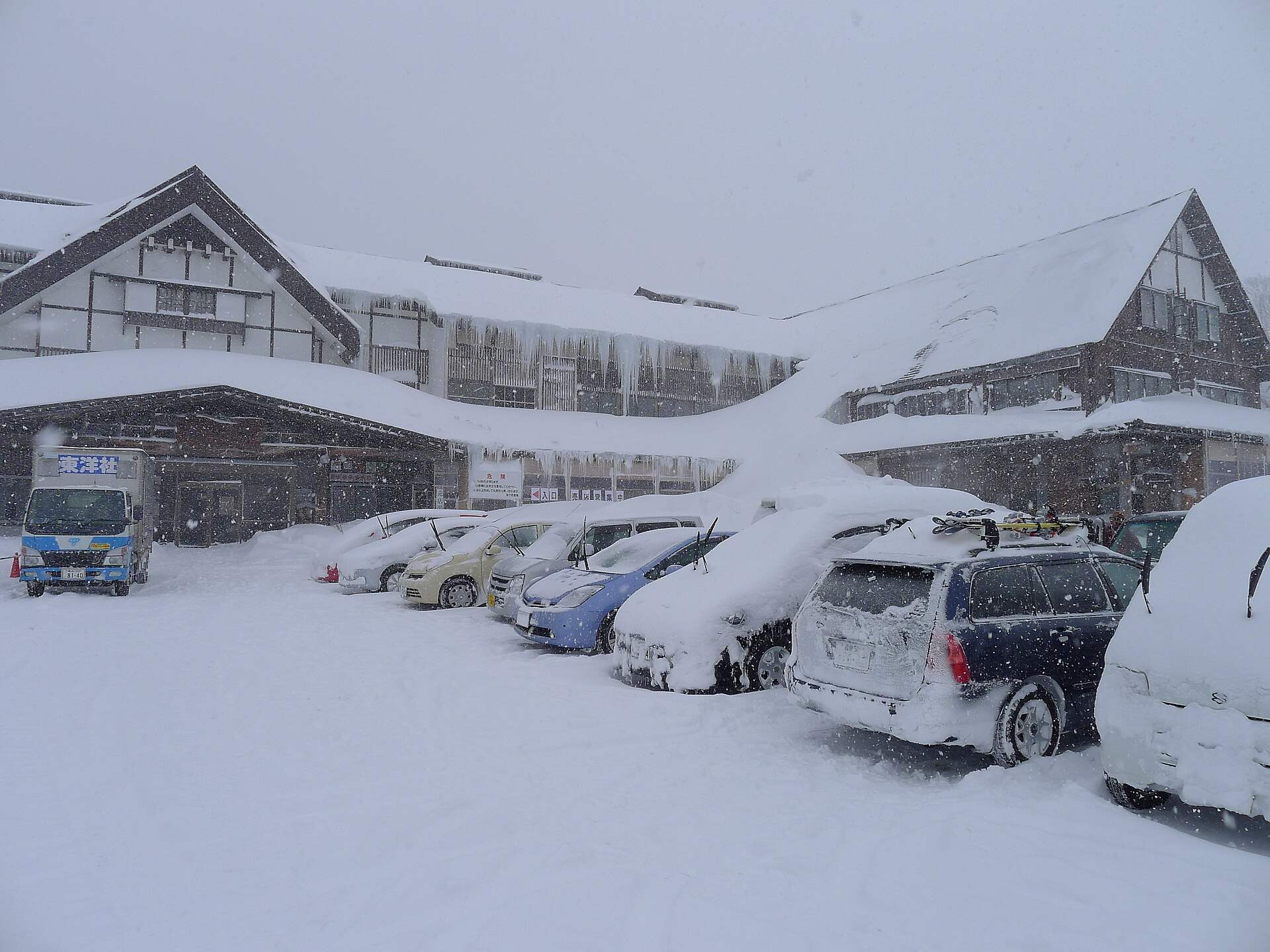 雪の降る冬の酸ヶ湯温泉の旅館の建物と雪に埋もれた駐車場