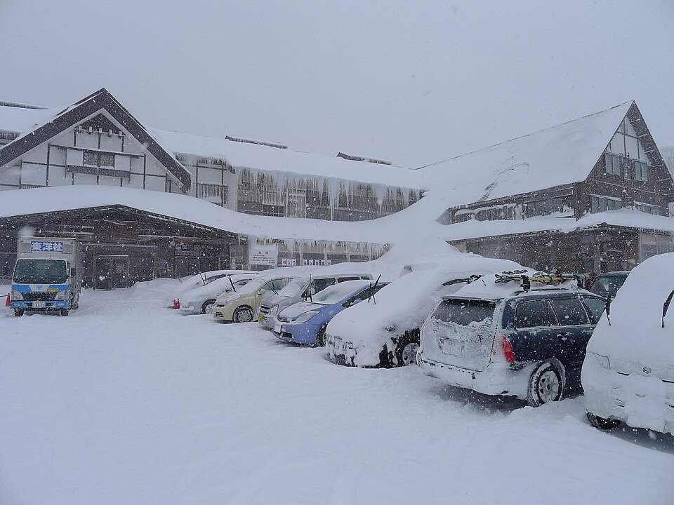雪の降る冬の酸ヶ湯温泉の旅館の建物と雪に埋もれた駐車場